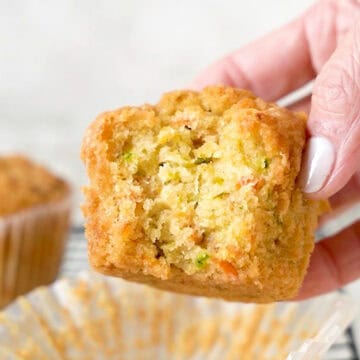 Holding a bitten carrot zucchini muffin. White background.