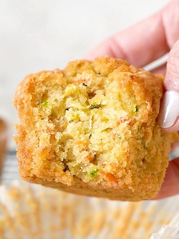 Holding a bitten carrot zucchini muffin. White background.