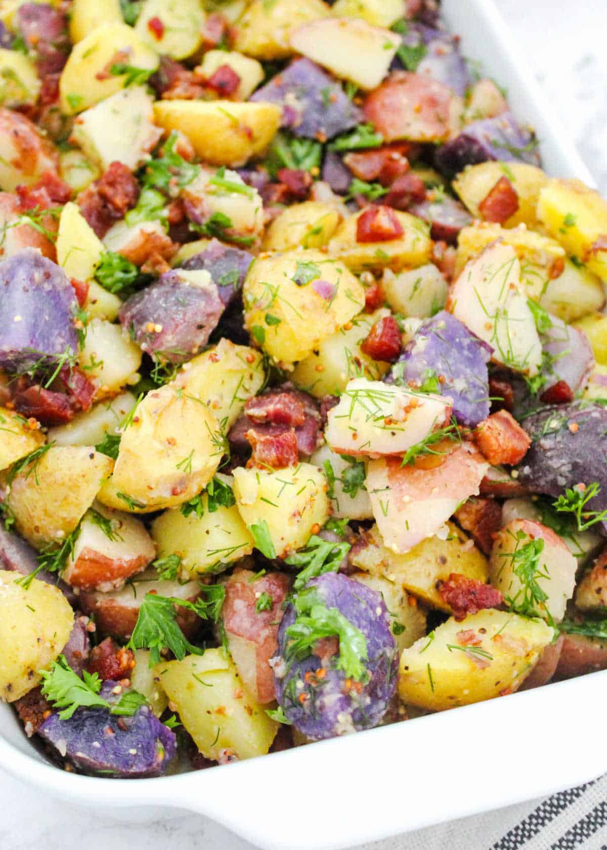 Close up of no mayo potato salad with bacon bits, herbs and different colored potatoes.
