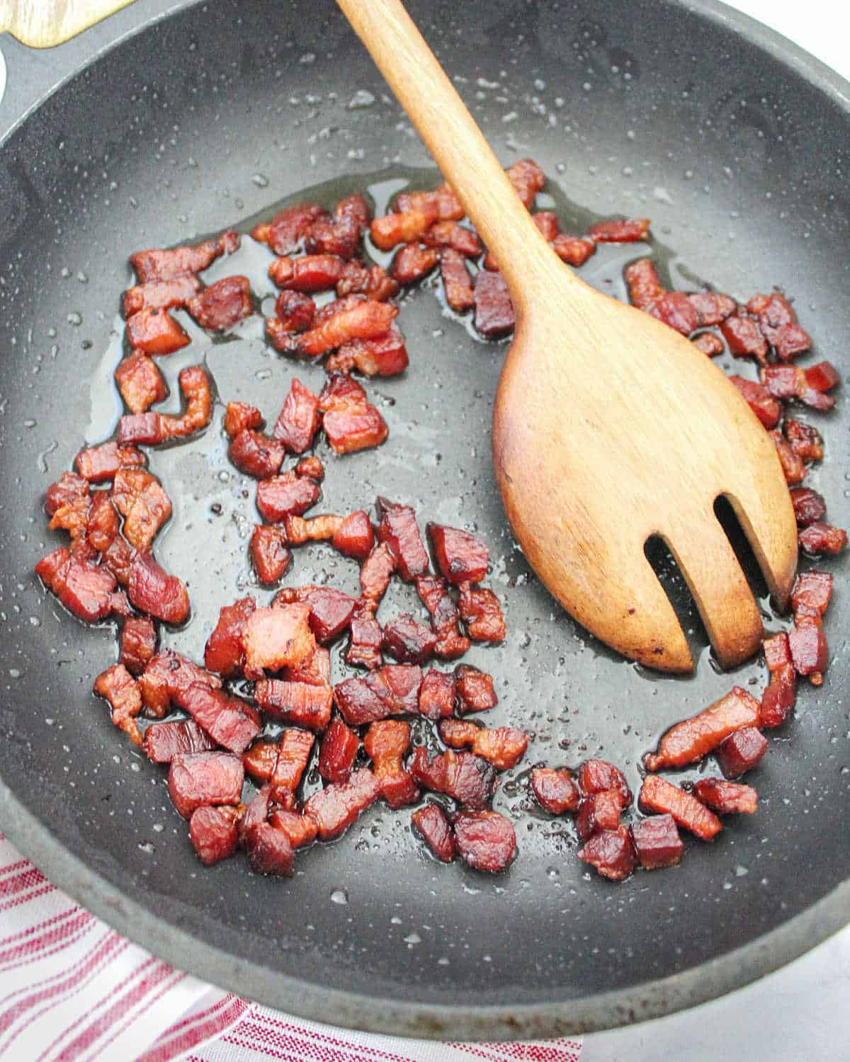 Bacon crispy bits in a dark skillet. Wooden spoon.