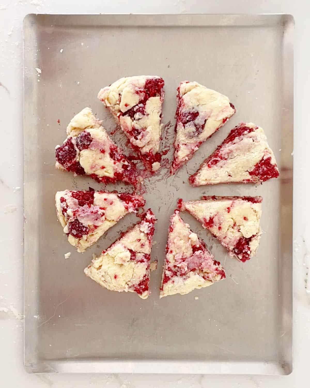 Eight raspberry scone triangles on a baking sheet. Top view.