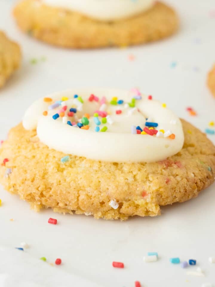 Close up of funfetti cookie with frosting. White surface with sprinkles.