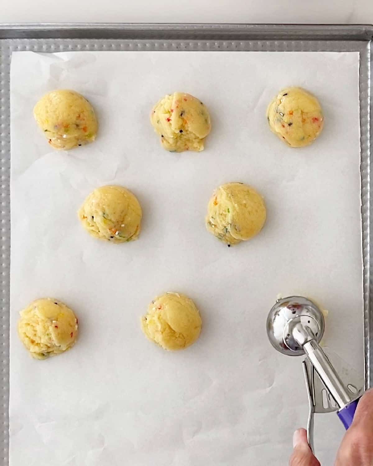 Scooping funfetti cookie balls on a parchment-lined sheet. To view.