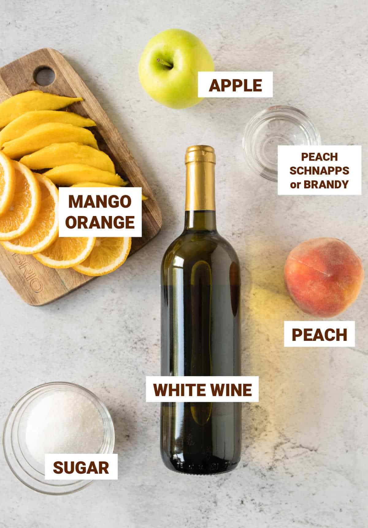 Grey background with ingredients for white wine sangria including summer fruit, sugar, apple, brandy.