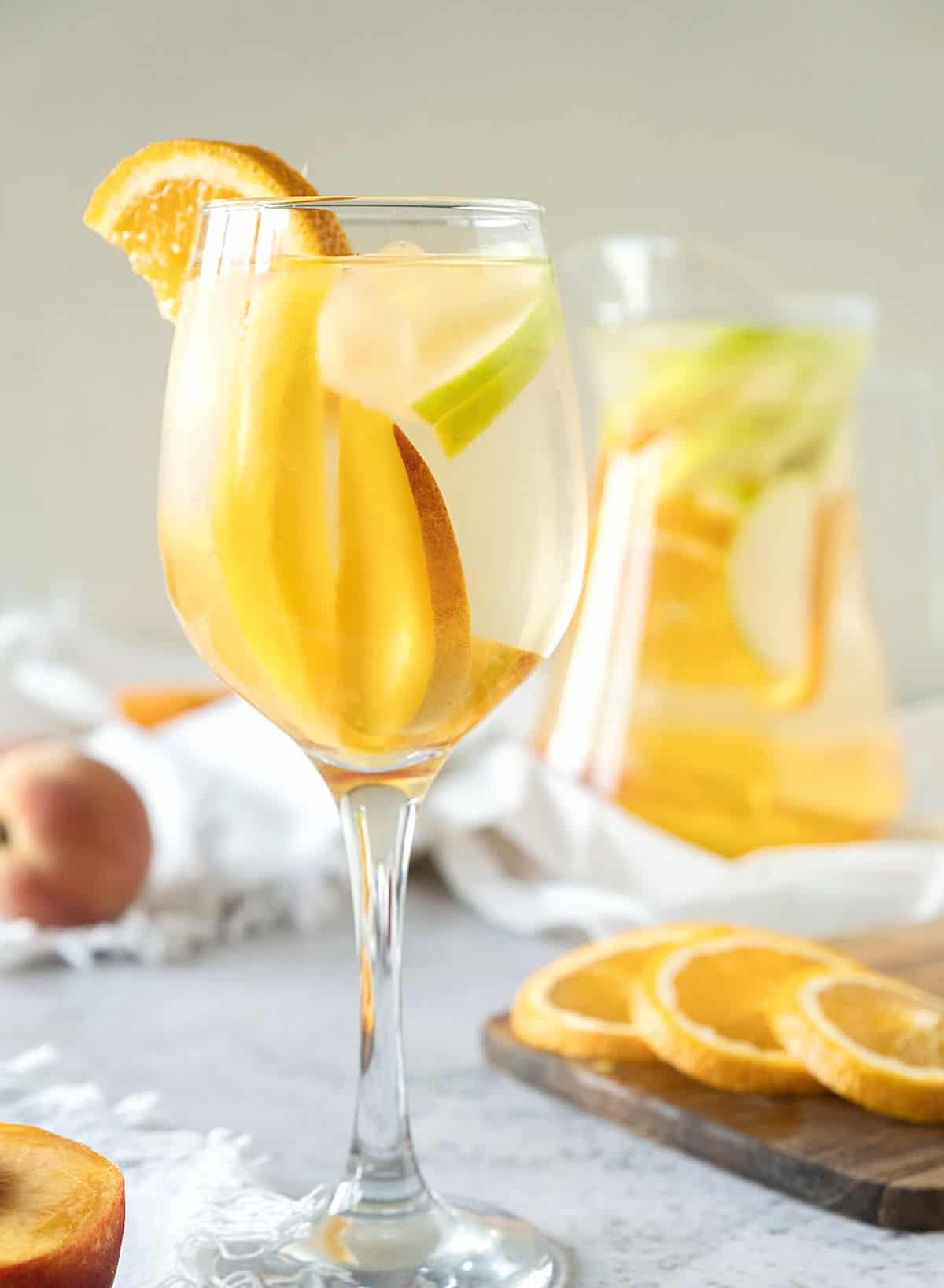 A beige background with white wine sangria in a pitcher and stem glass.