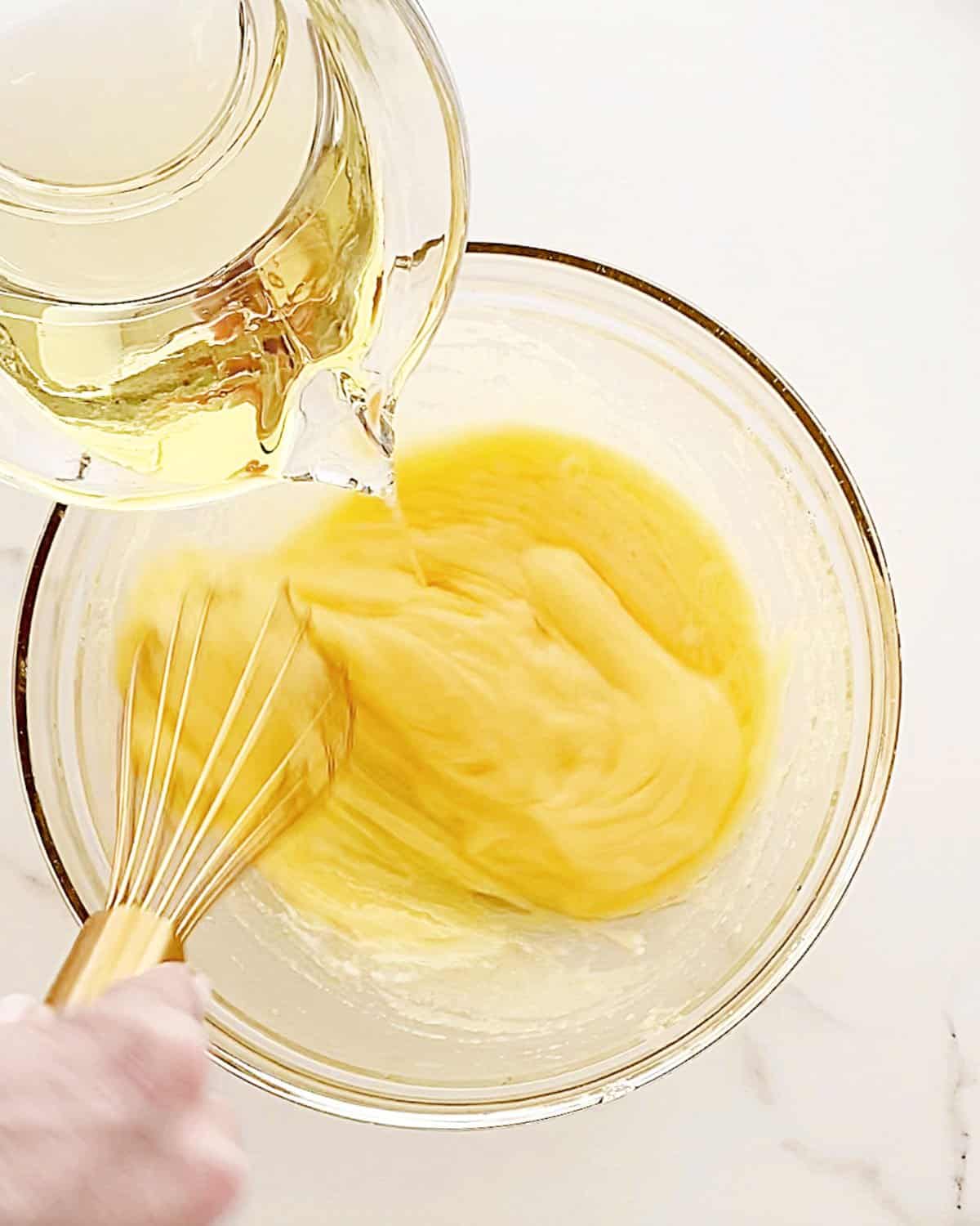 Adding oil from a glass jar onto sugar in a glass bowl. White marbled surface. 