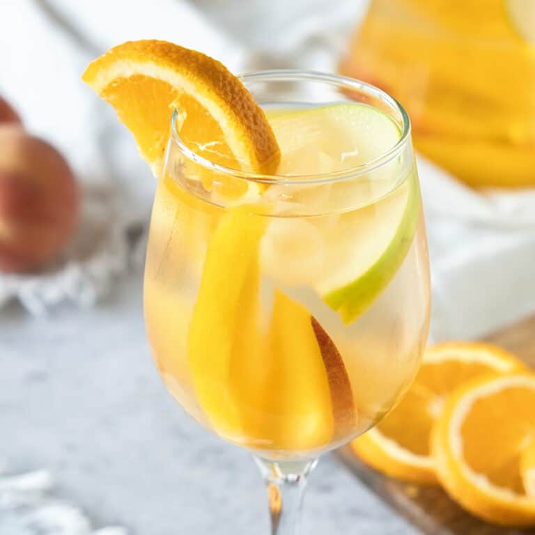 A stem glass with white wine sangria, orange slice. Grey surface, fruit pieces.