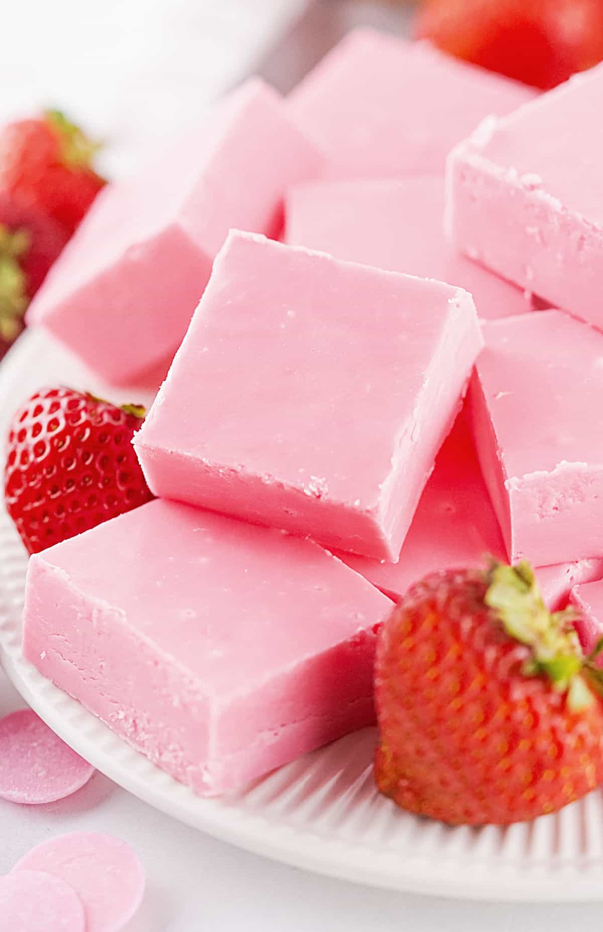 Close up pile of strawberry fudge squares on a white plate with fresh strawberries.