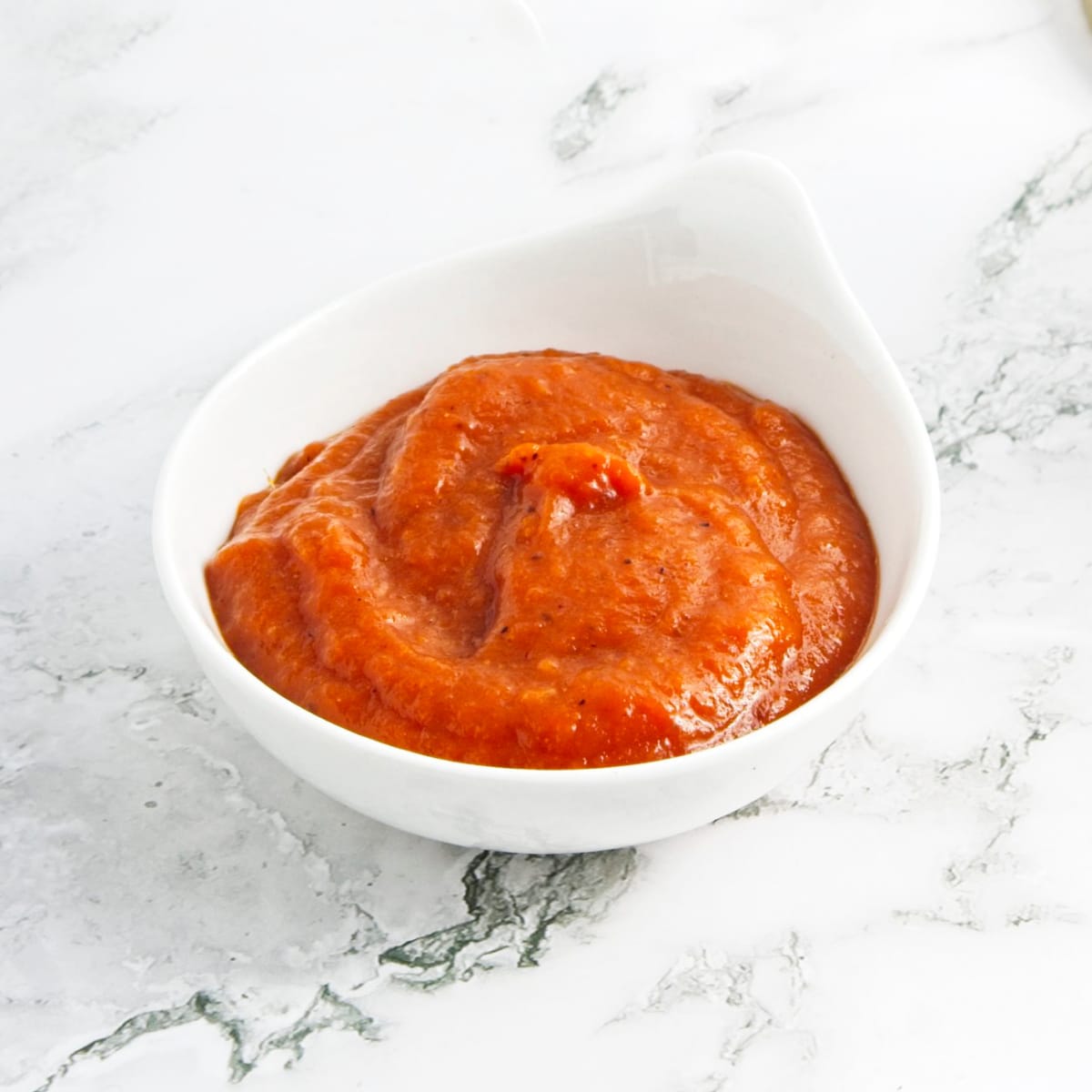 White bowl with homemade ketchup. White marbled surface.