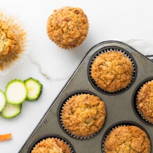 Zucchini carrot muffins in metal pan and white marbled surface. Zucchini slices.