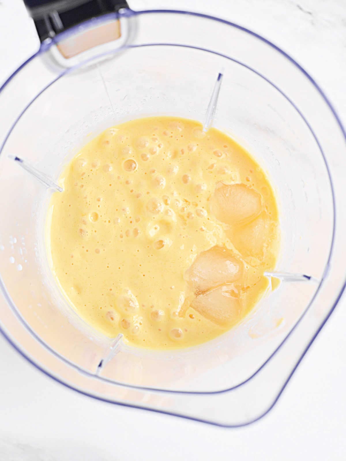 Top view of blender jar with mango milkshake mixture. White surface.
