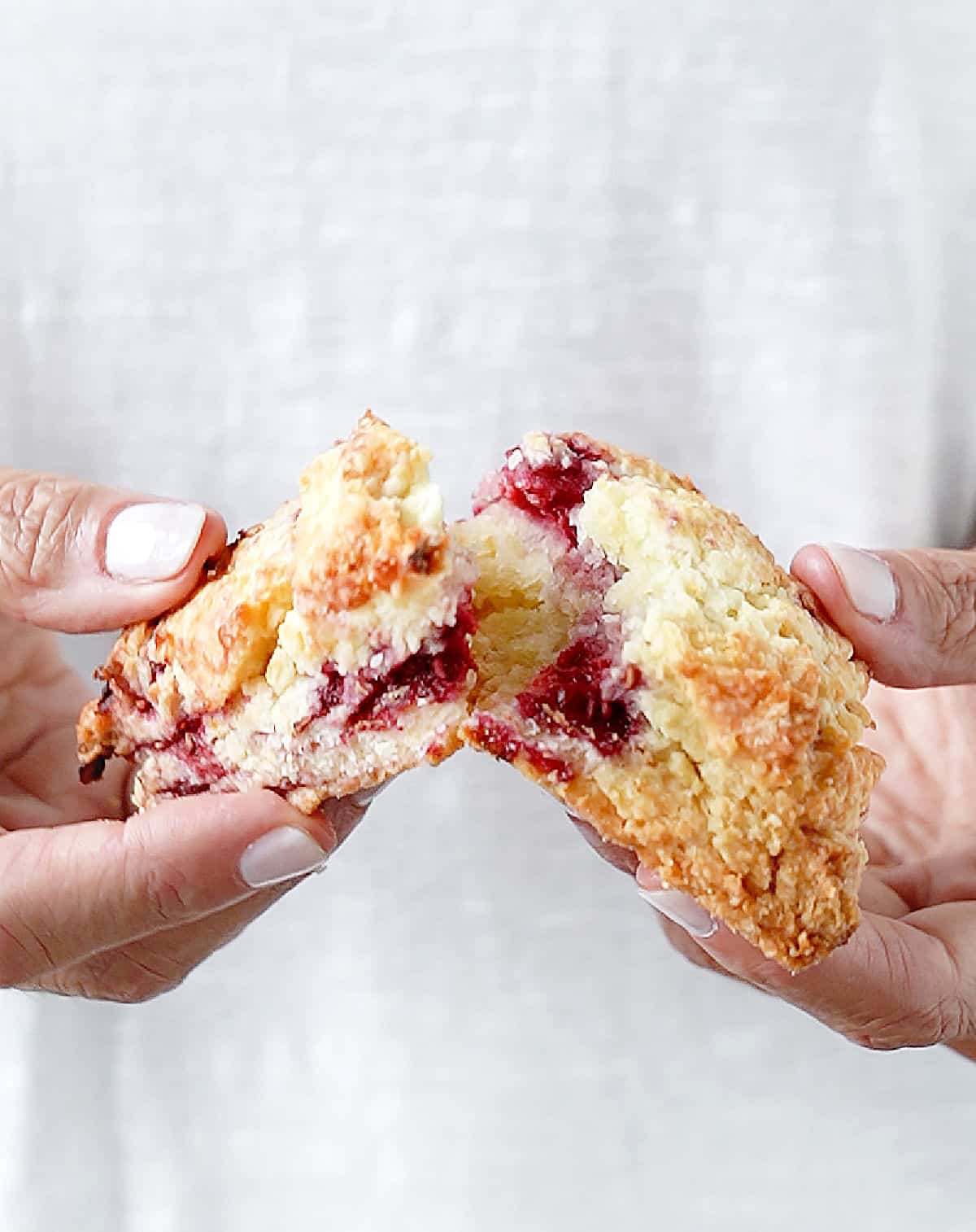Hands opening a fresh raspberry scone. White background. 