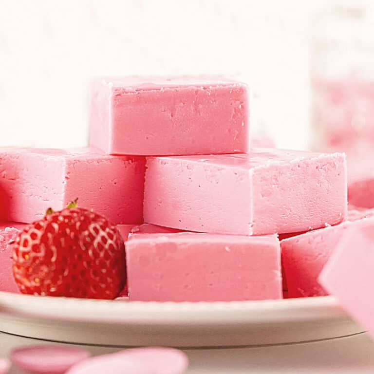 Stacked strawberry fudge squares on a white plate with a fresh strawberry. White background.