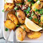 Bacon potato salad with green onions. White plate, lemon wedge.