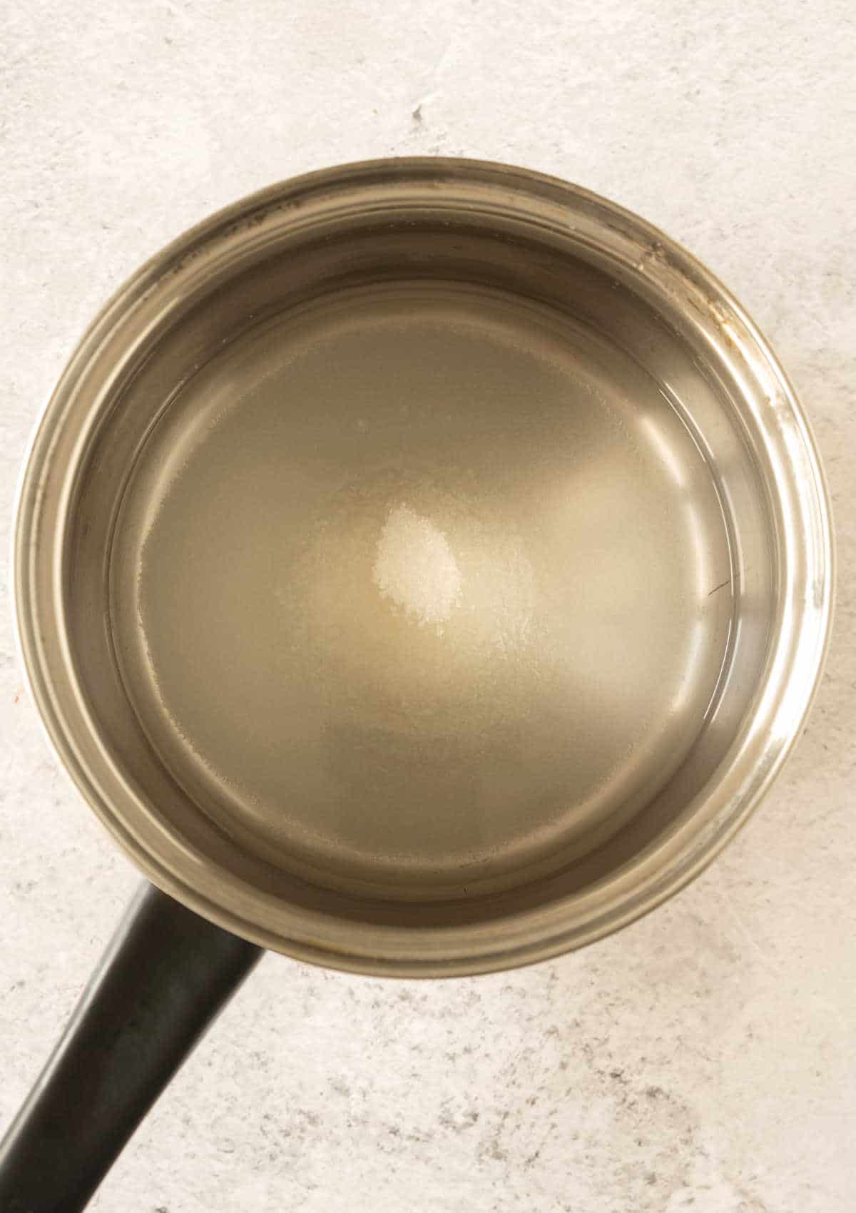 Top view of metal saucepan with water and sugar. Greyish surface.