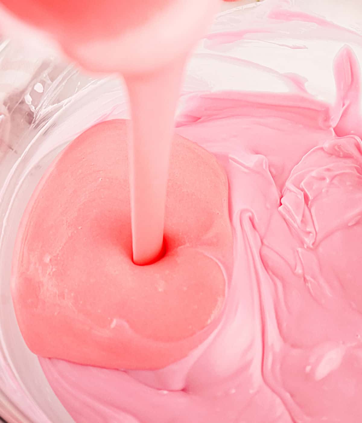 Pouring thin pink frosting into glass bowl with melted pink chocolate.