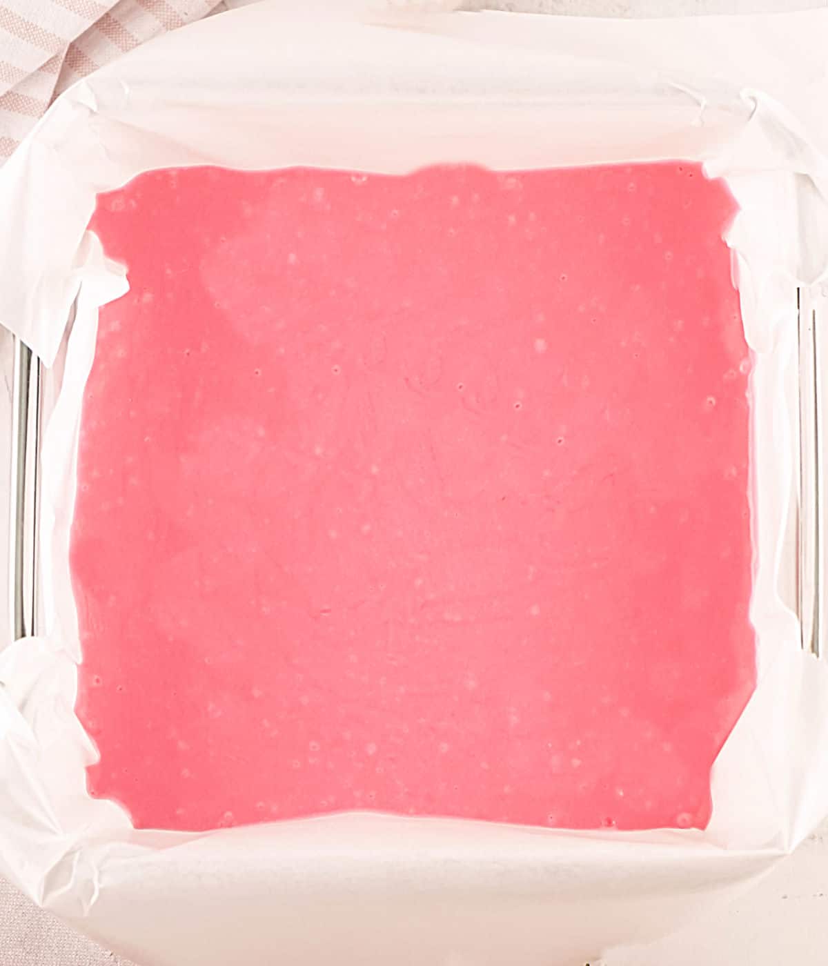 Parchment paper lined square pan with pink strawberry fudge before solidifying.