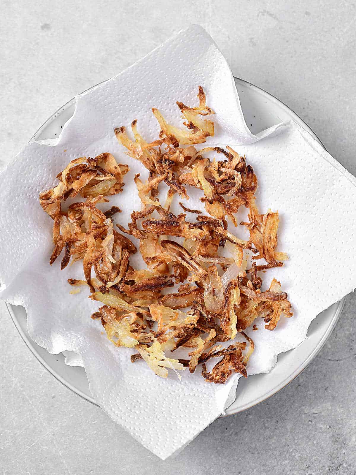 Crispy onions blotting on white paper towels. Light grey surface.