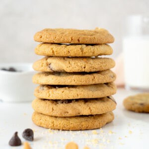 Stack of several chocolate chip cookies. White marble surface. Light grey background with milk bottle and bowl.