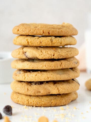 Stack of several chocolate chip cookies. White marble surface. Light grey background with milk bottle and bowl.