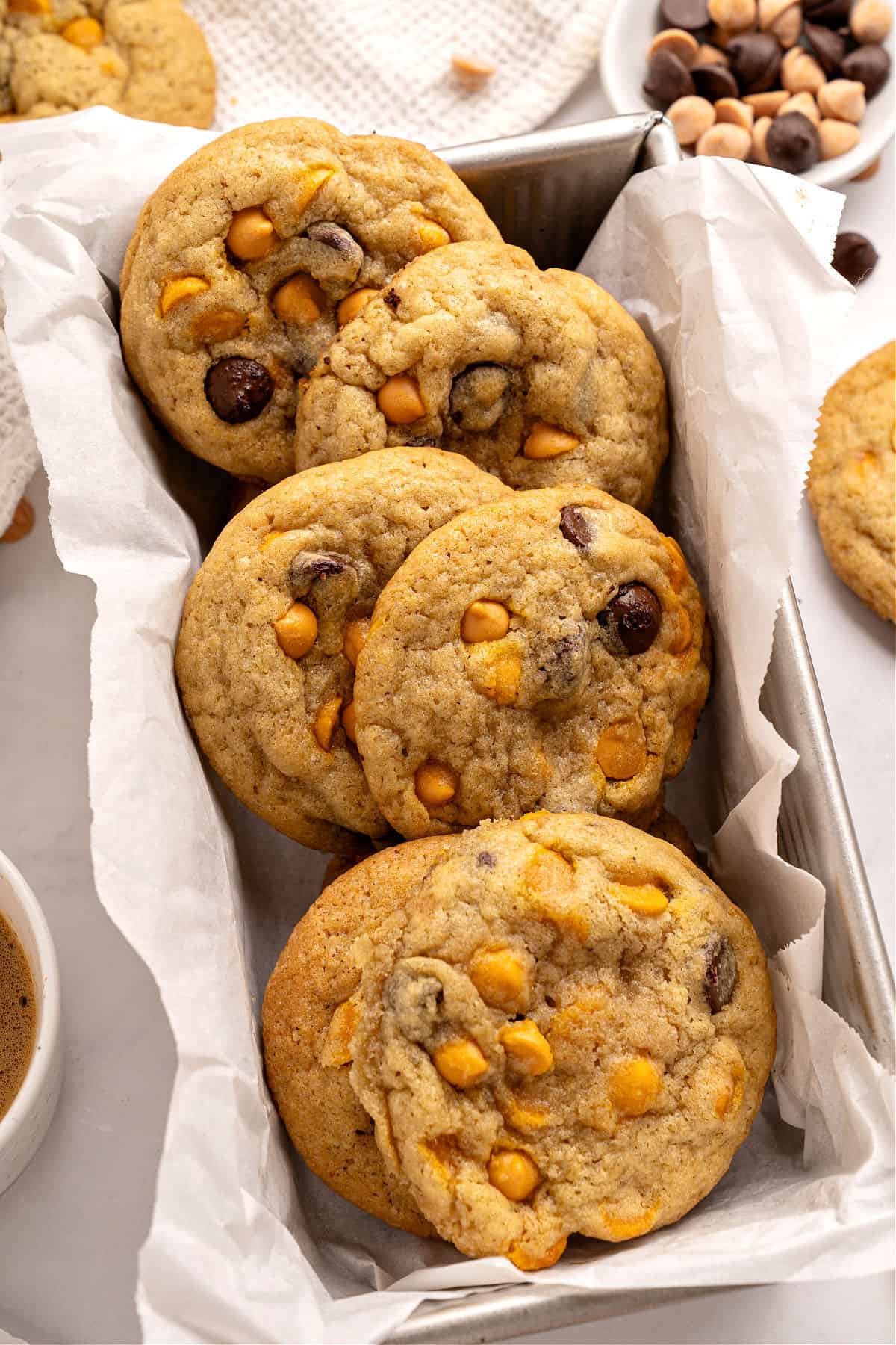 Several chocolate butterscotch chip cookies on white paper in a metal loaf pan.
