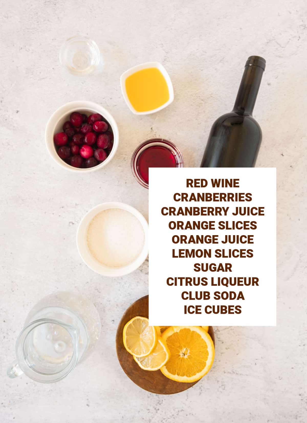 Light grey background with ingredients for cranberry sangria including sugar, ice cubes, citrus slices, cranberry juice.