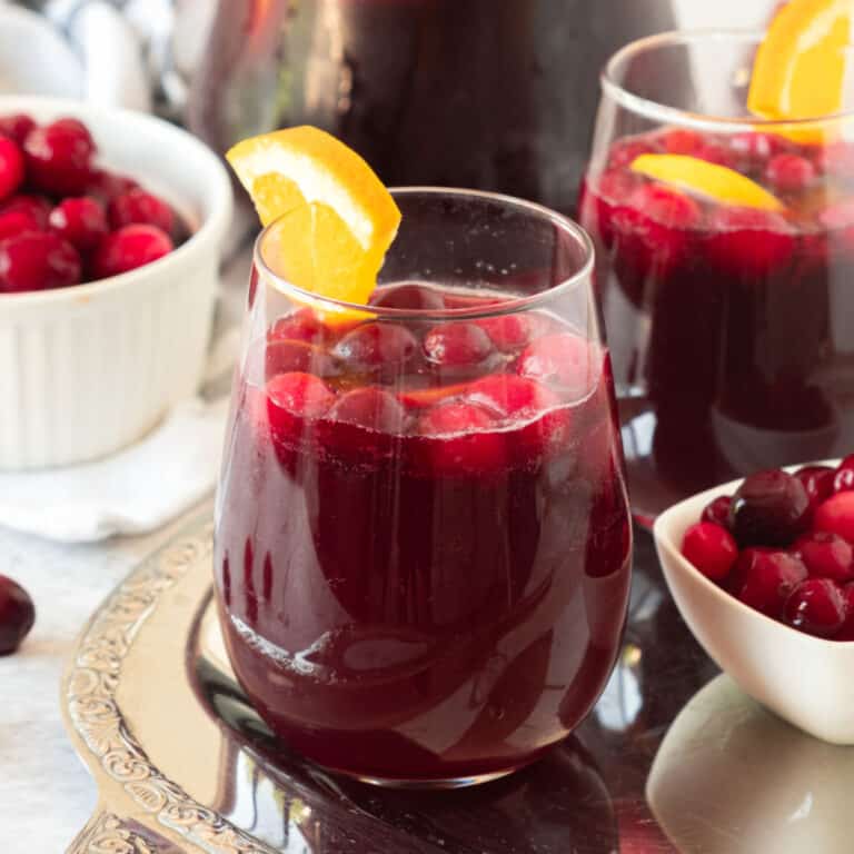 Two glasses of cranberry sangria with orange on a metal tray. White bowls with cranberries.