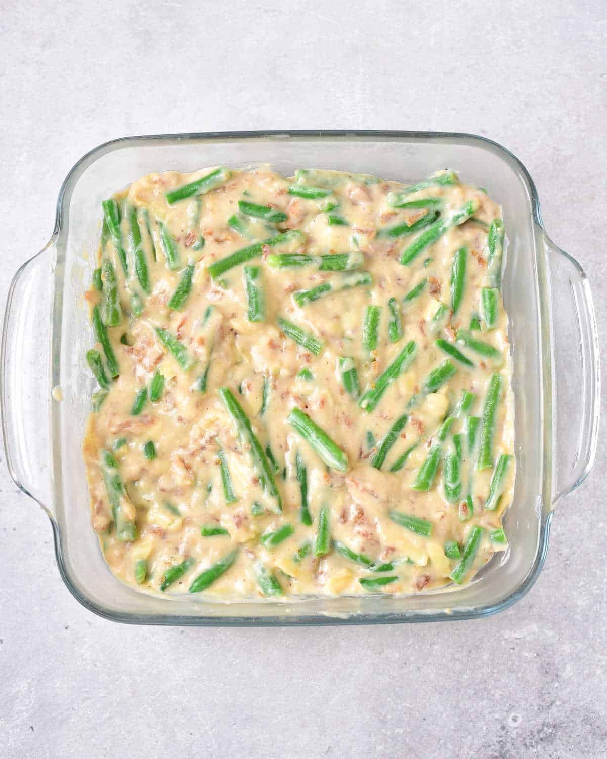 Glass dish with green bean casserole before baking on a grey surface.