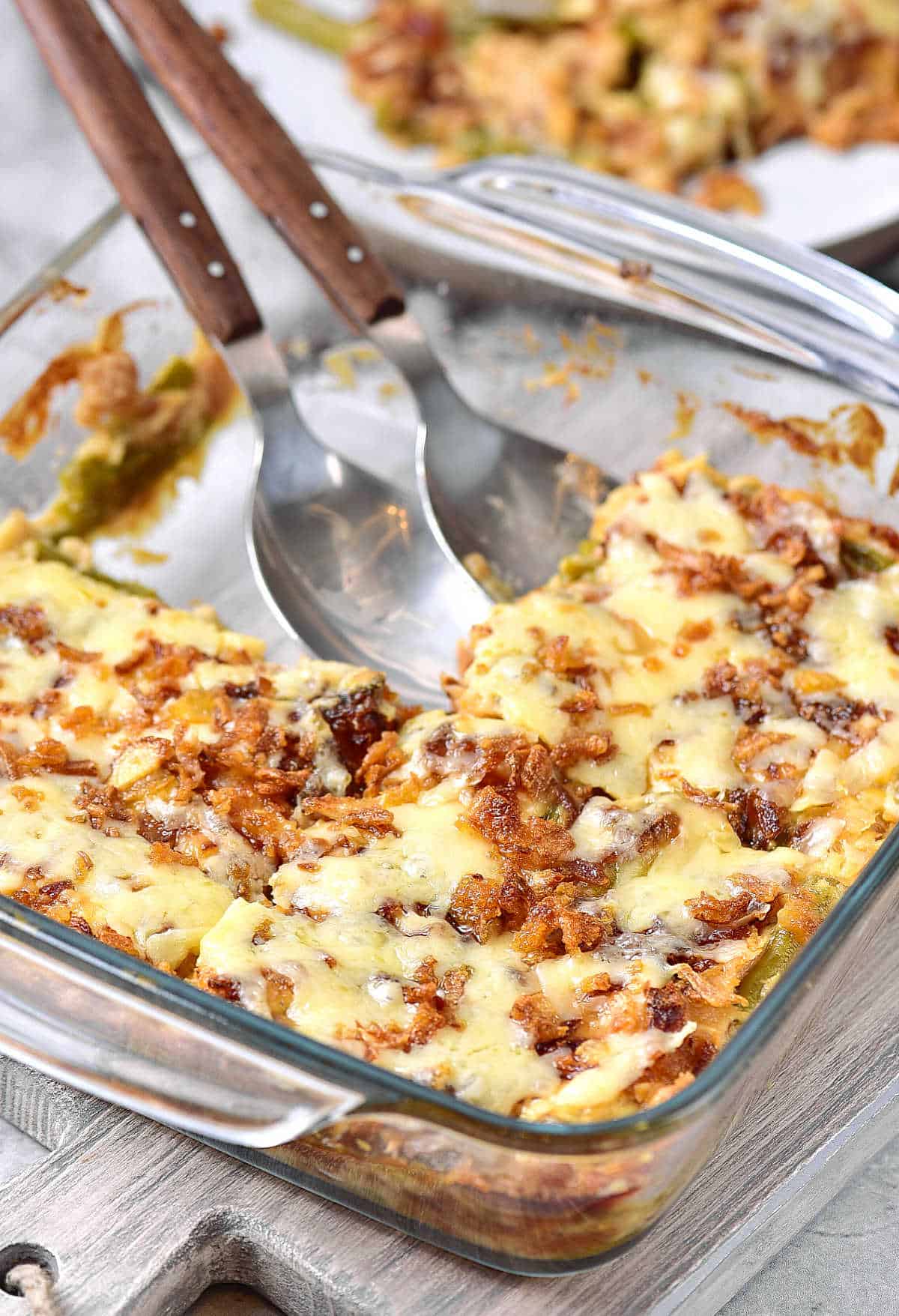 Two serving spoons in a glass bowl with cheese and onion topped casserole. 