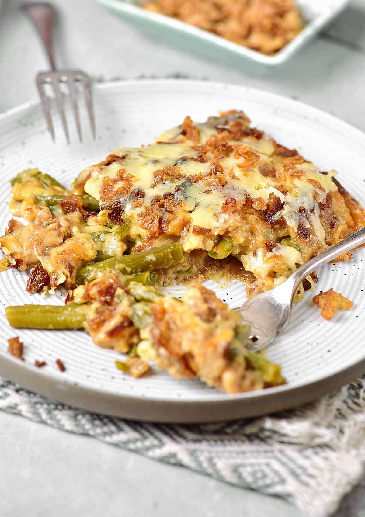 Onion topped green bean casserole serving on a white plate. Silver forks. 