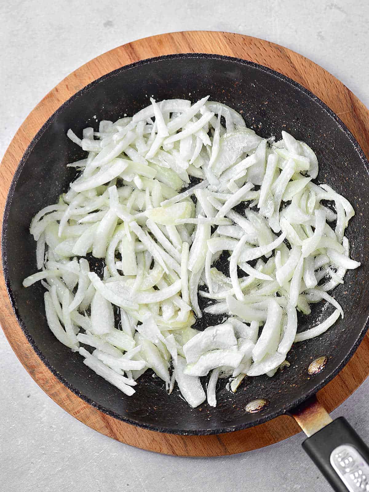 Sliced onions in a black skillet on a wooden board. Light grey surface. 
