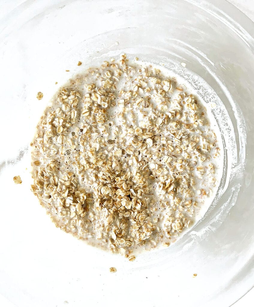 Oats and milk in a glass bowl on a white surface. Top view.