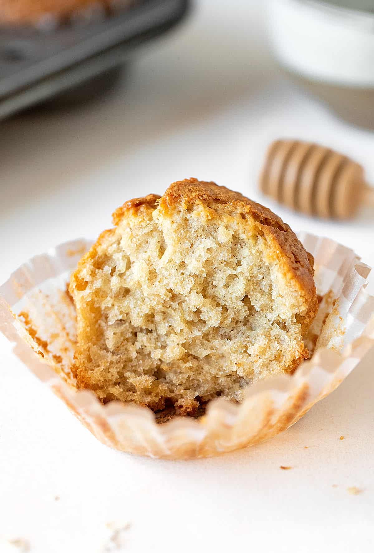 Half eaten oatmeal muffin on an opened paper liner, white surface.