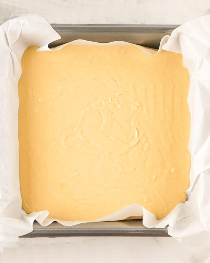 Top view of metal square pan with parchment paper and peanut butter fudge mixture.