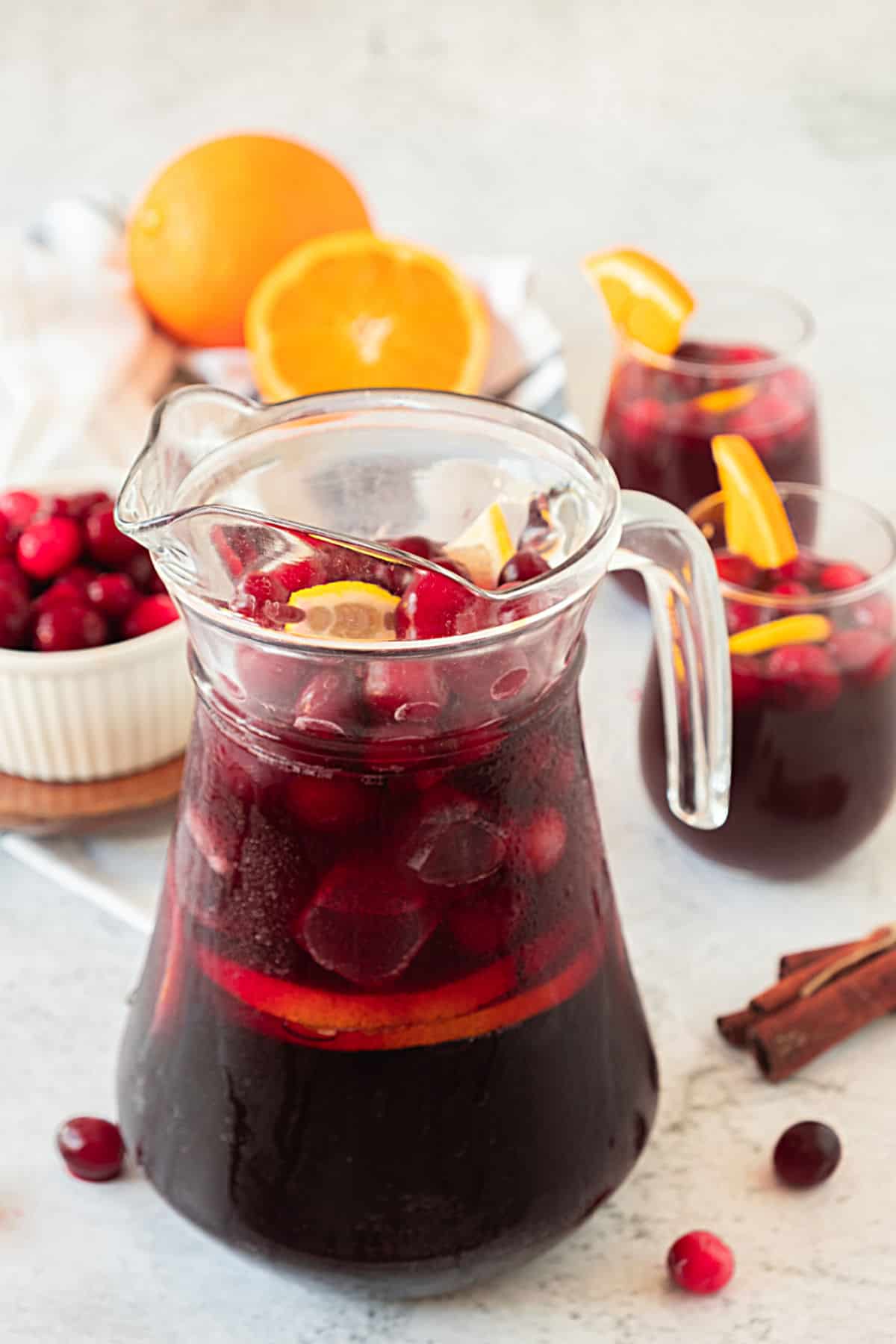 Filled pitcher with cranberry sangria with orange. Light colored surface and background. Orange slices, fresh cranberries.