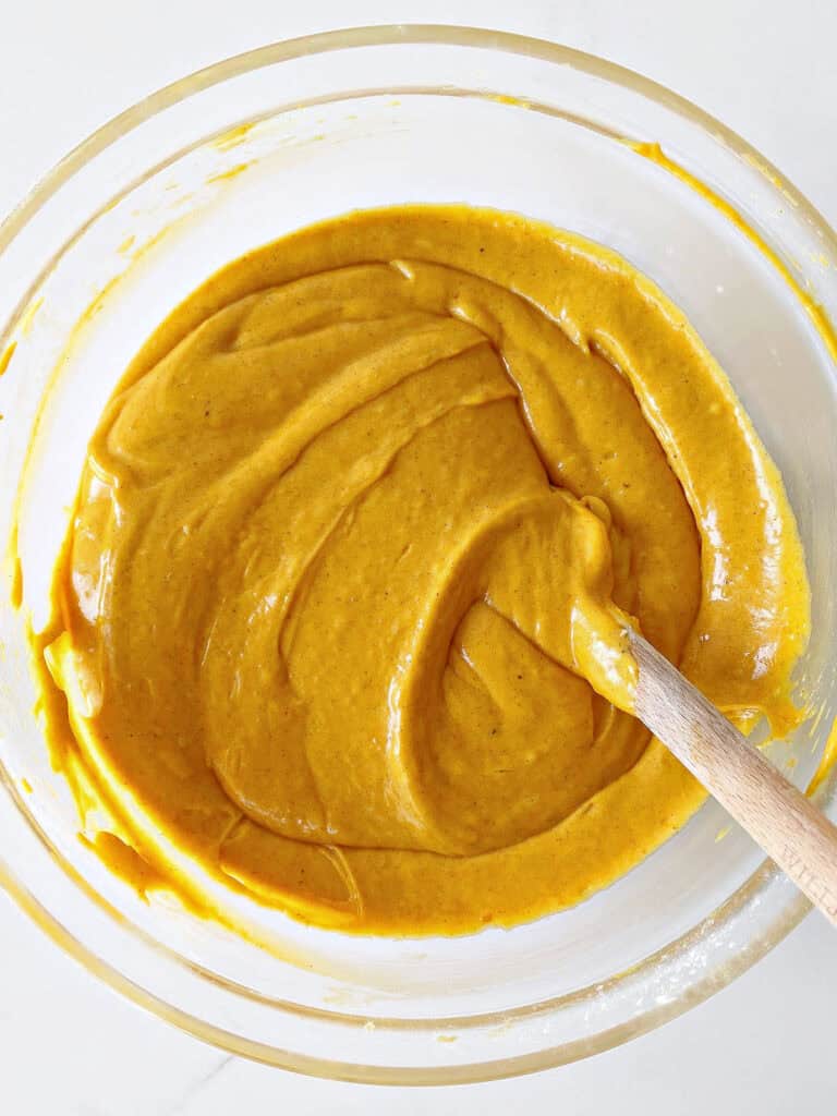 Glass bowl with pumpkin cake batter. A spatula. White surface. Top view.