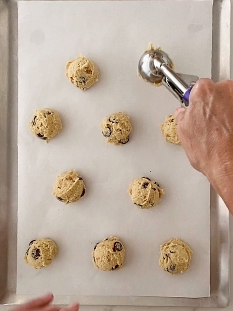 Scooping cookies on a parchment lined baking sheet. Top view.