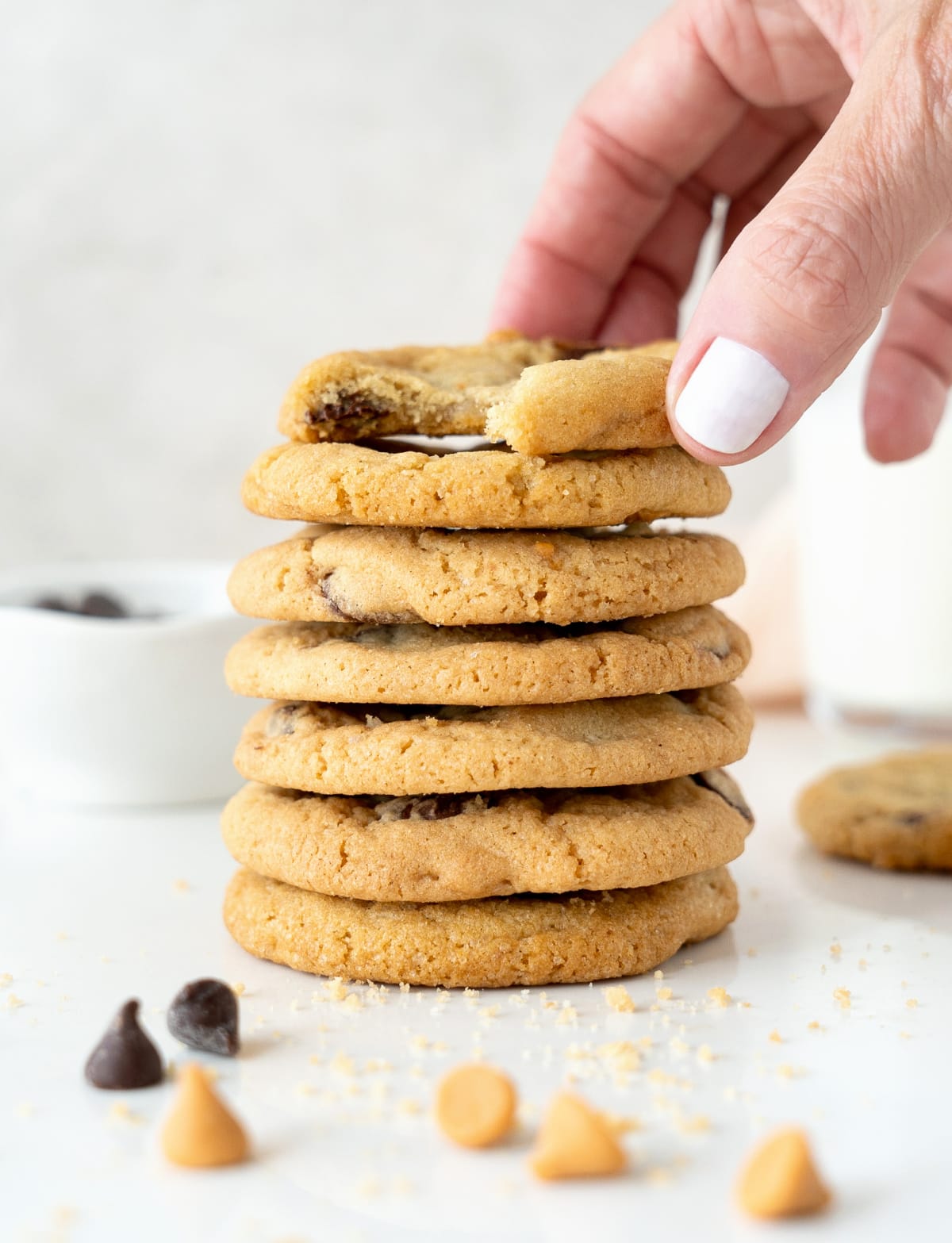 Lifting bitter chocolate chip cookie from a stack. White surface and background. Loose chips. 