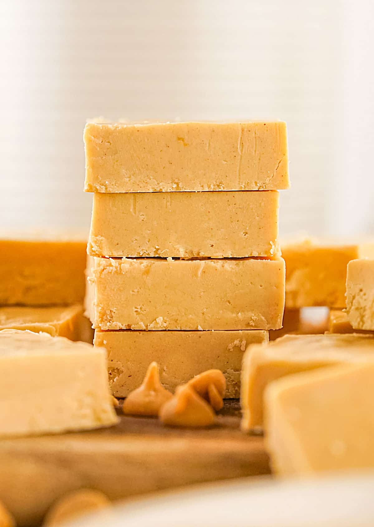 Stack of four peanut butter fudge pieces on a wooden surface. More squares around. White background.