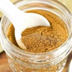 Close up mason jar with apple pie spice and a white ceramic spoon inside.