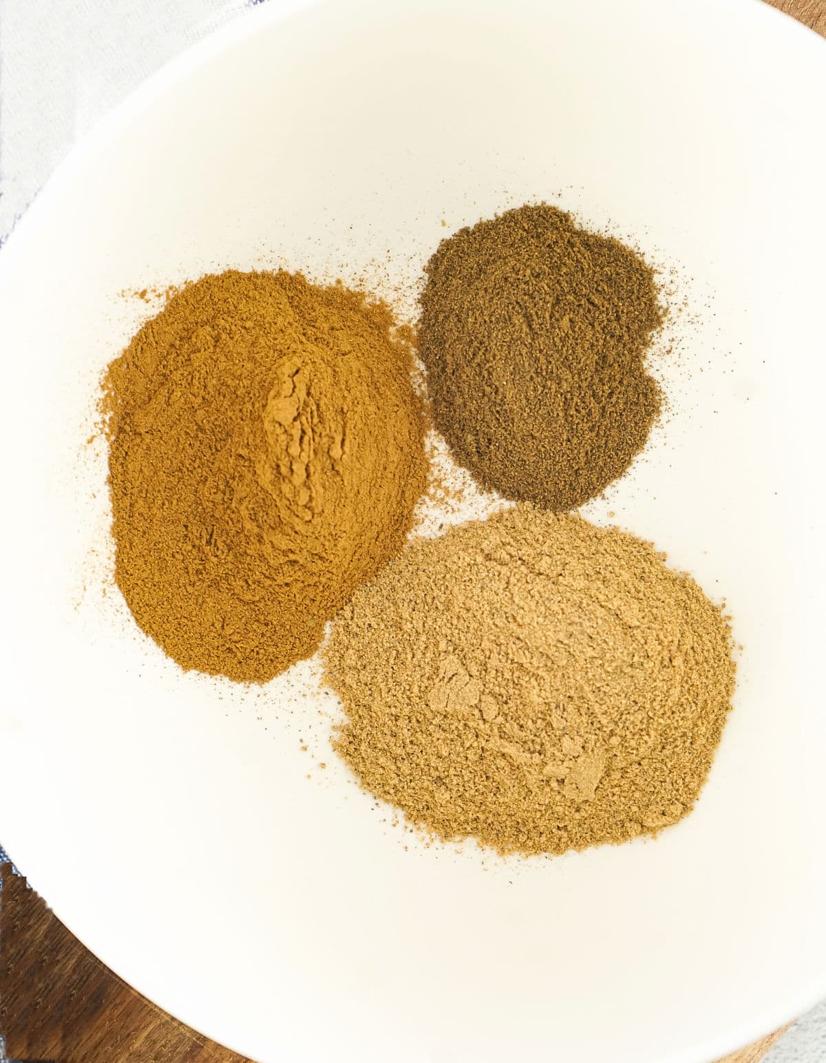 Mounds of ground cinnamon, nutmeg and allspice in a white bowl.