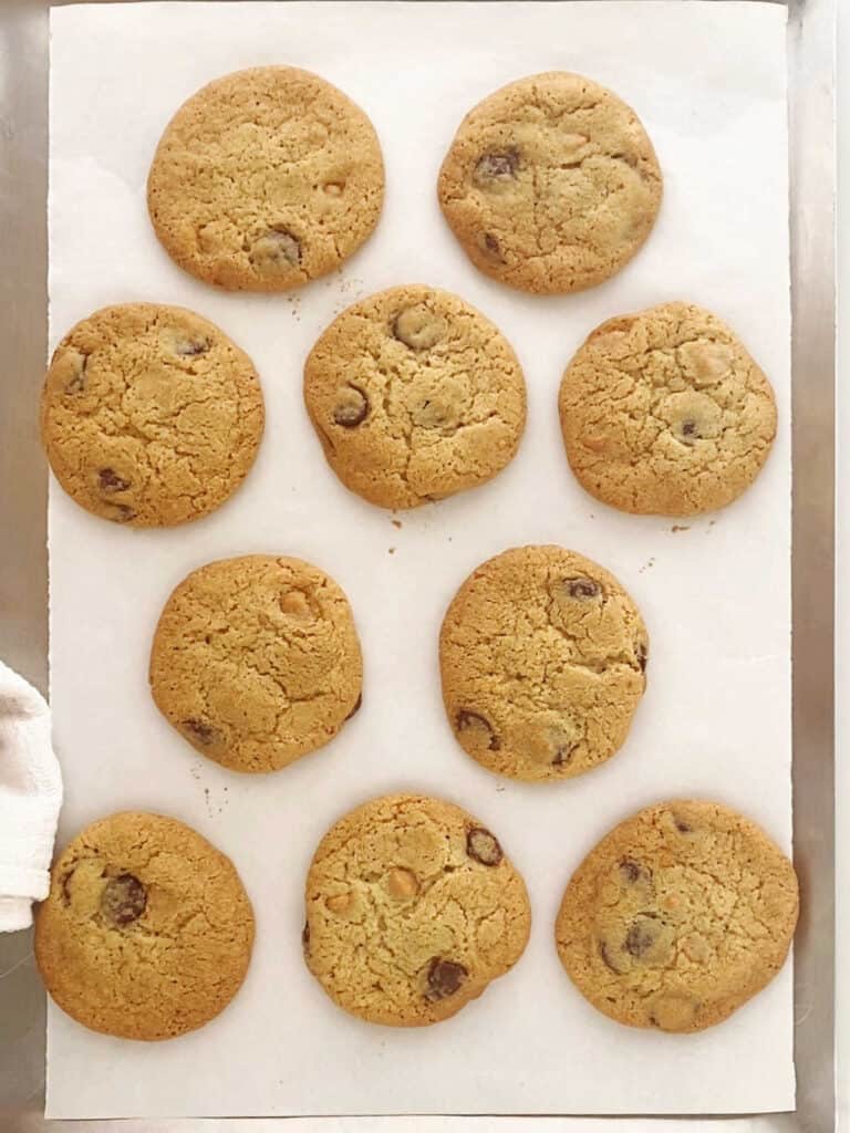 Baked chocolate chip butterscotch cookies on a white parchment-lined cookie sheet.