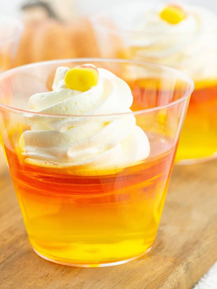 Wooden board with orange and yellow jello cups with a dollop of whipped cream.