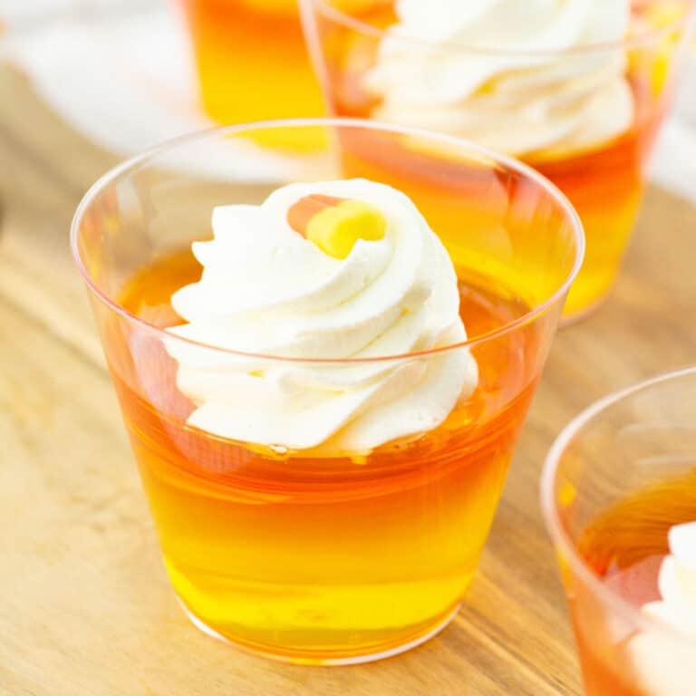 Close up of orange and yellow jello cups with whipped cream. Wooden board surface.