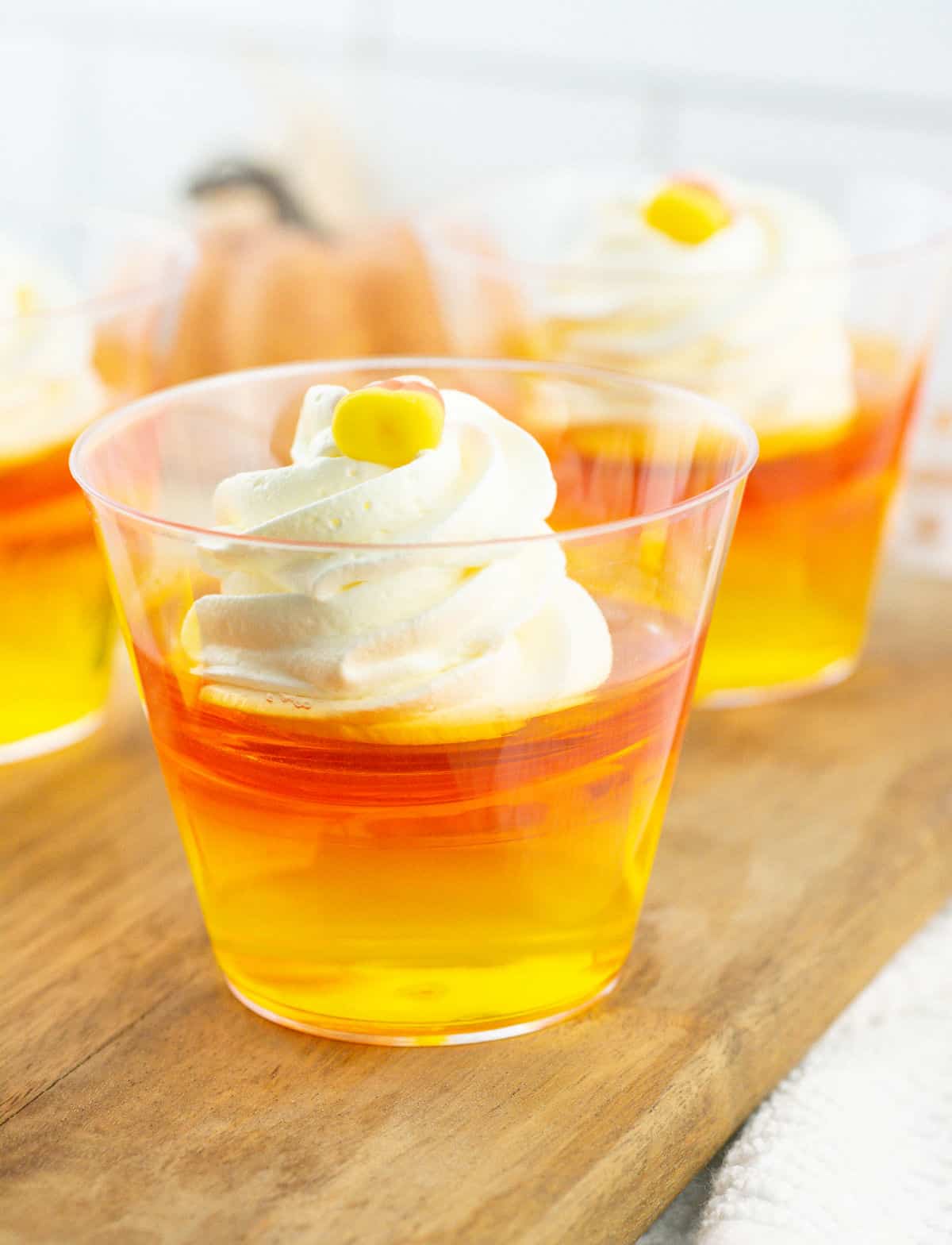Cups of orange and yellow jello cups with a dollop of whipped cream. Wooden board surface. 