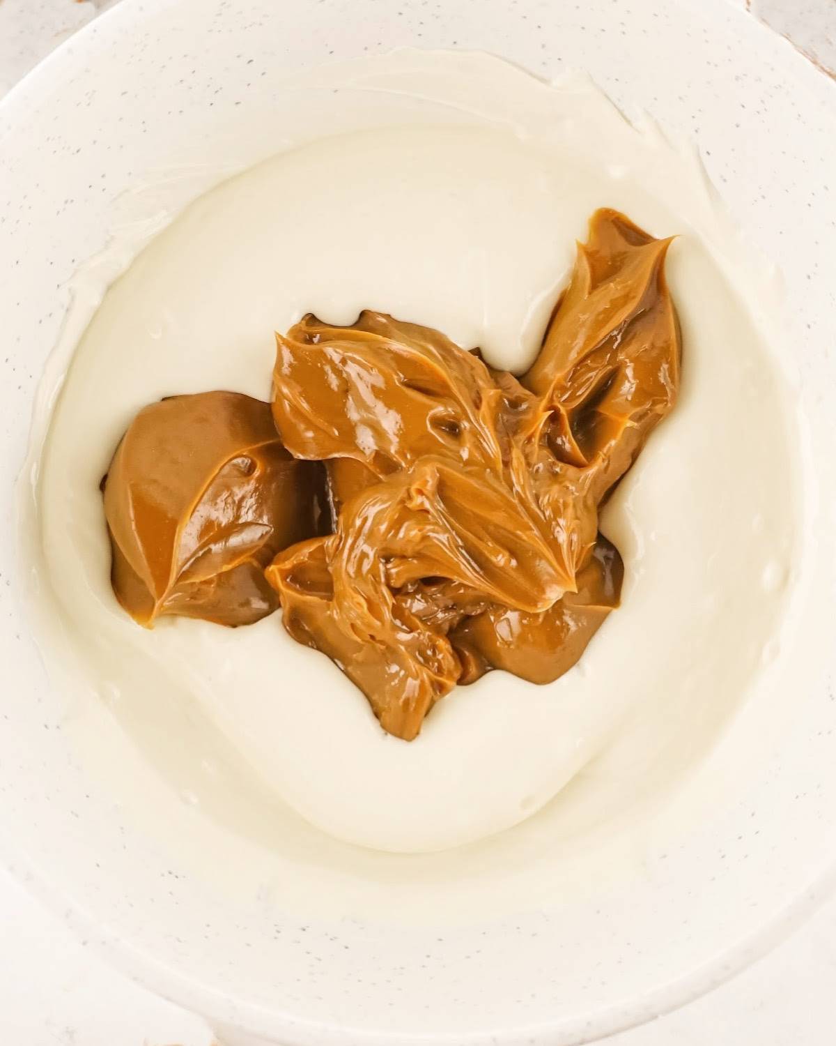 Melted white chocolate and dulce de leche before mixing in a white shallow bowl.