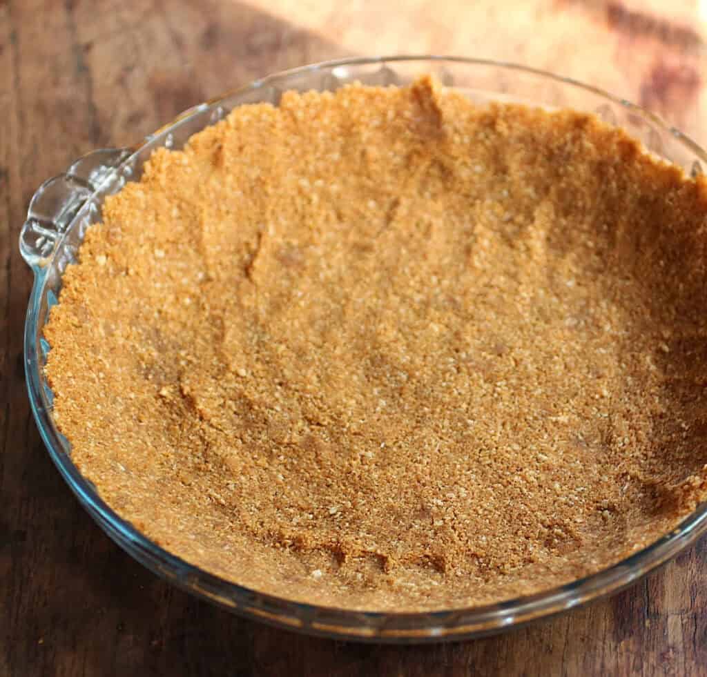 Glass pie plate with pressed cookie crust, wooden table.