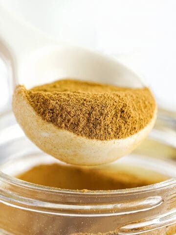 White spoon lifting apple pie spice mix from a jar. White background.