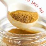 Red and white text overlay on white spoon with apple pie spice lifted from a mason jar.