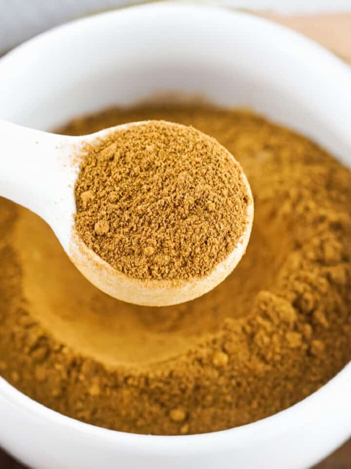 Pumpkin spice mix in a white bowl with a white round spoon lifting some of it.